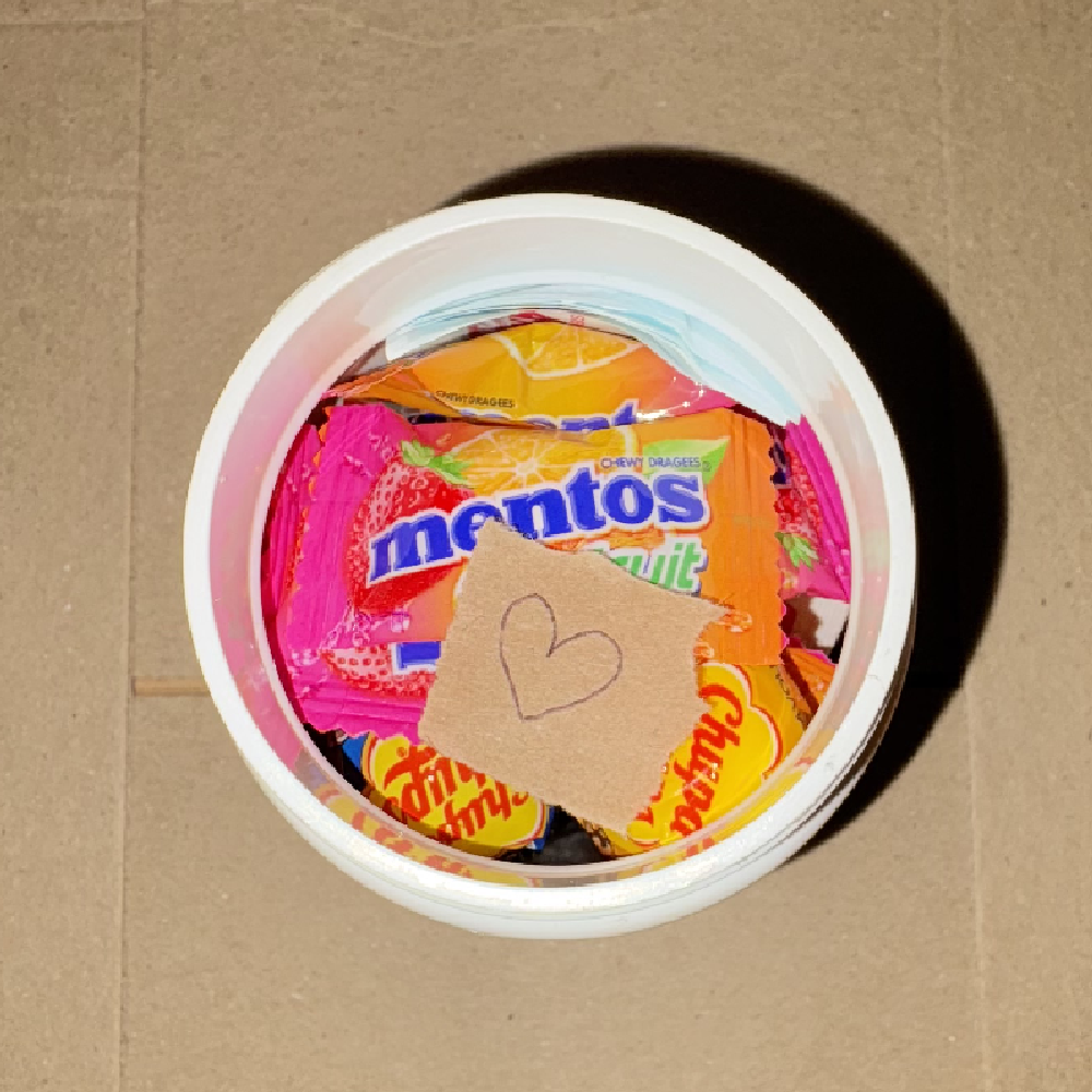 Brown paper heart note resting on top of lollies inside the capsule tub.